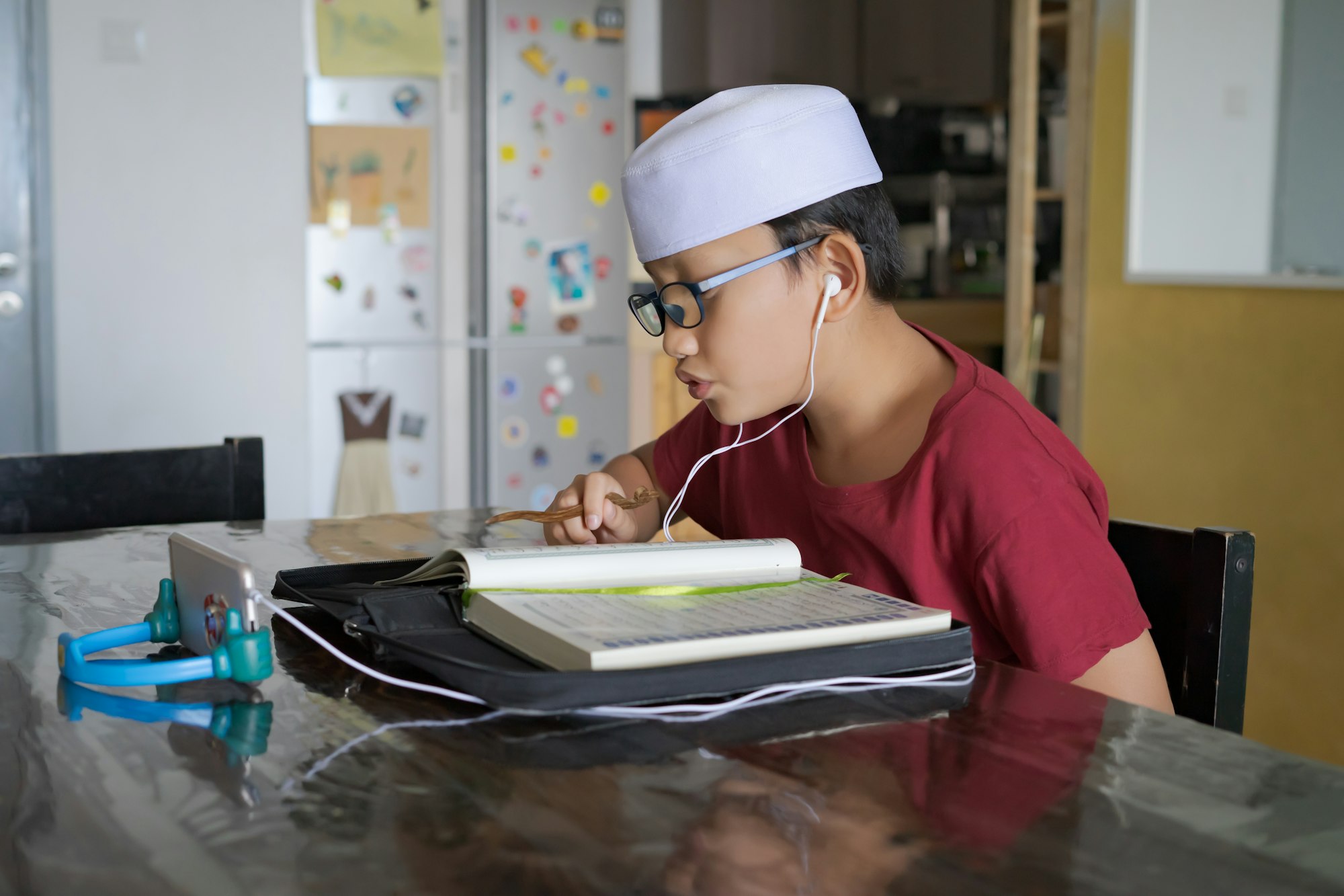 Asian kid reading Al-Quran through video call using smartphone during education and learning from ho